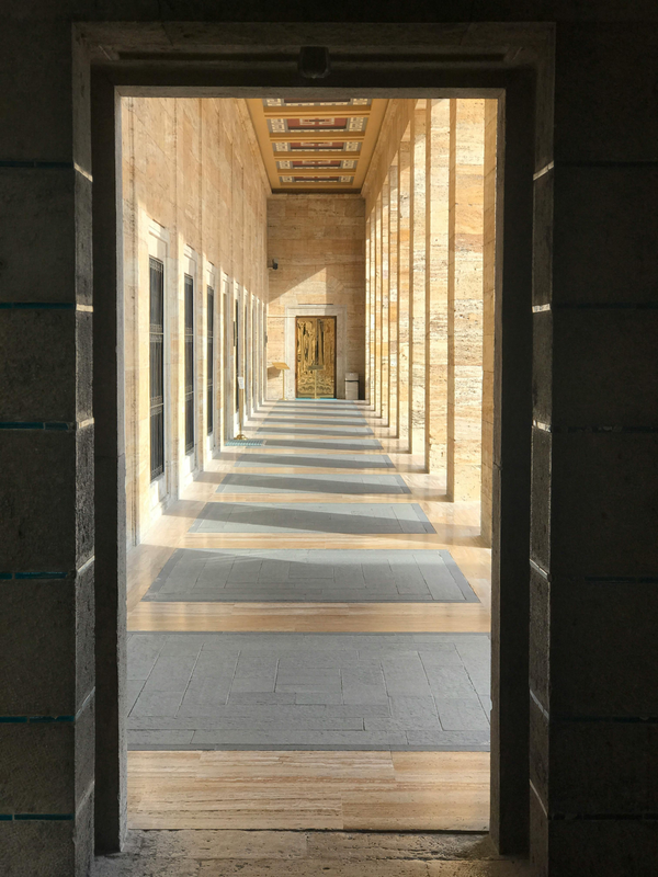 Sunlit stone corridor with repeating columns and distant doorway, expressing architectural order, symmetry, and calm institutional design.